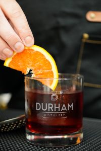 A classic negroni being garnished with fresh orange slices.