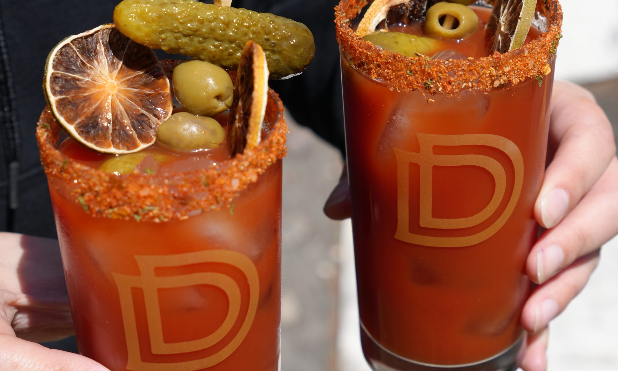 Two Canadian Caesar cocktails in tall highball glasses with garnishes