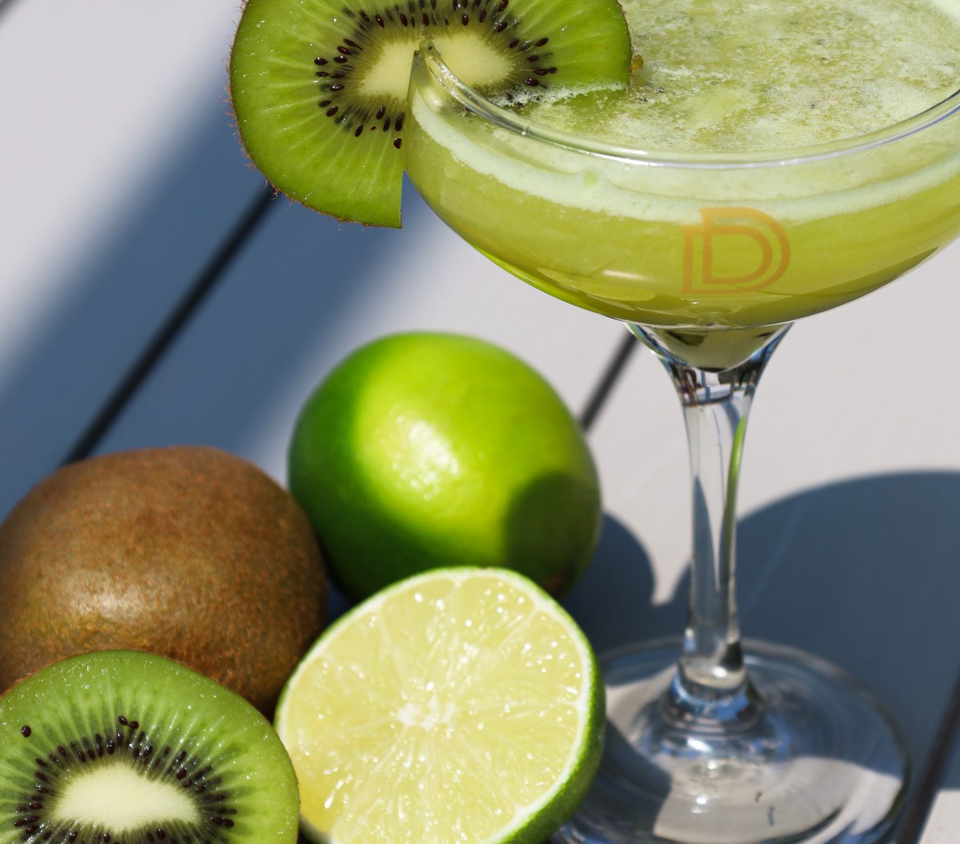A refreshing Flightless Bird cocktail served in a chilled glass, garnished with fresh kiwi slices and lime, showcasing its vibrant green hue