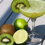 A refreshing Flightless Bird cocktail served in a chilled glass, garnished with fresh kiwi slices and lime, showcasing its vibrant green hue