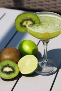 A refreshing Flightless Bird cocktail served in a chilled glass, garnished with fresh kiwi slices and lime, showcasing its vibrant green hue