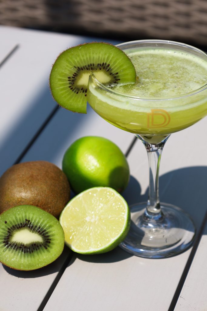 A refreshing Flightless Bird cocktail served in a chilled glass, garnished with fresh kiwi slices and lime, showcasing its vibrant green hue